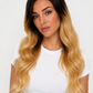 A woman with long, wavy ombre hair in dark brown to golden blonde, wearing a white t-shirt against a plain white background.