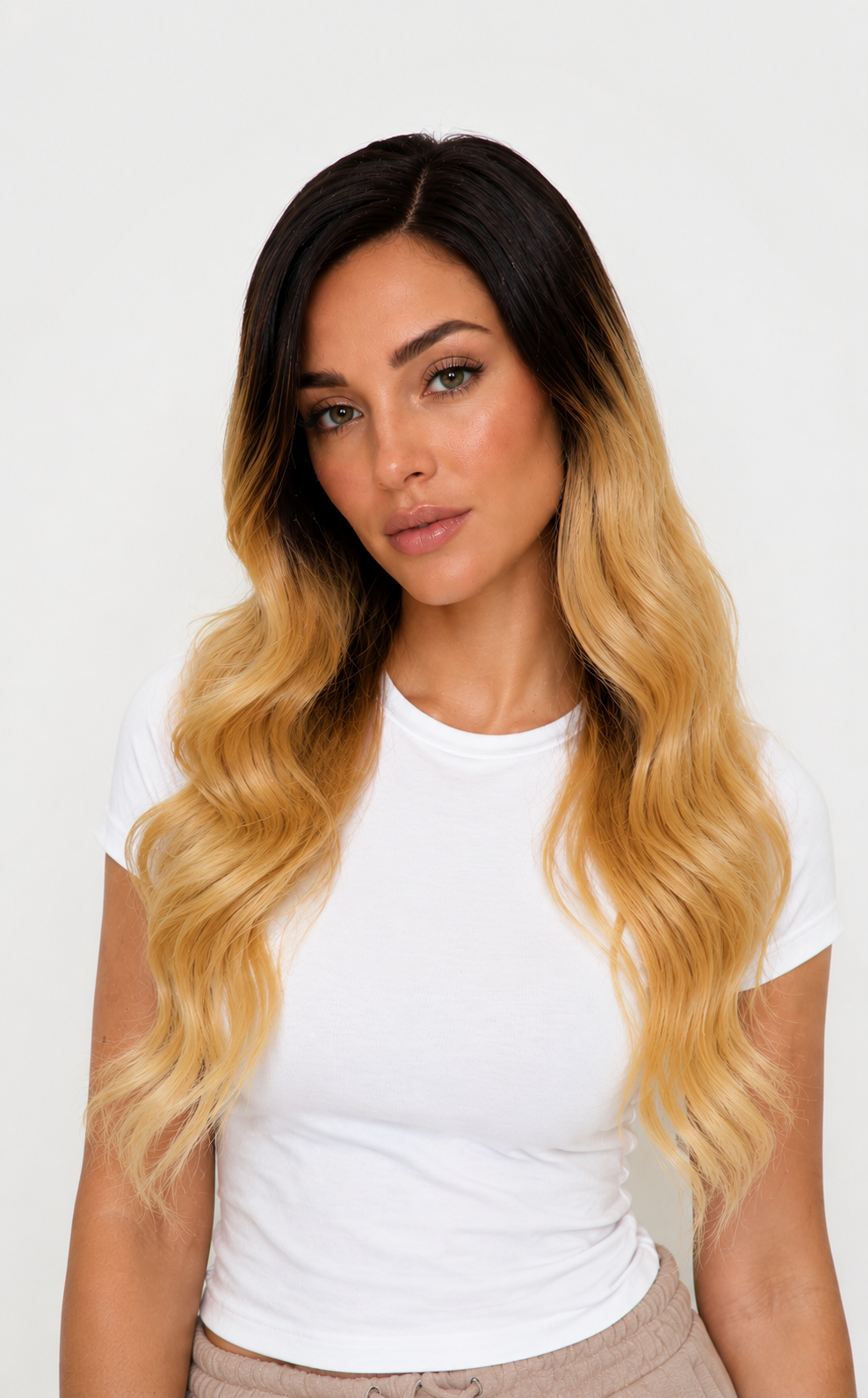 A woman with long, wavy ombre hair in dark brown to golden blonde, wearing a white t-shirt against a plain white background.