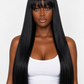 A woman with long, straight, black hair and straight bangs, wearing a white tank top and light blue jeans, photographed against a plain light gray background.