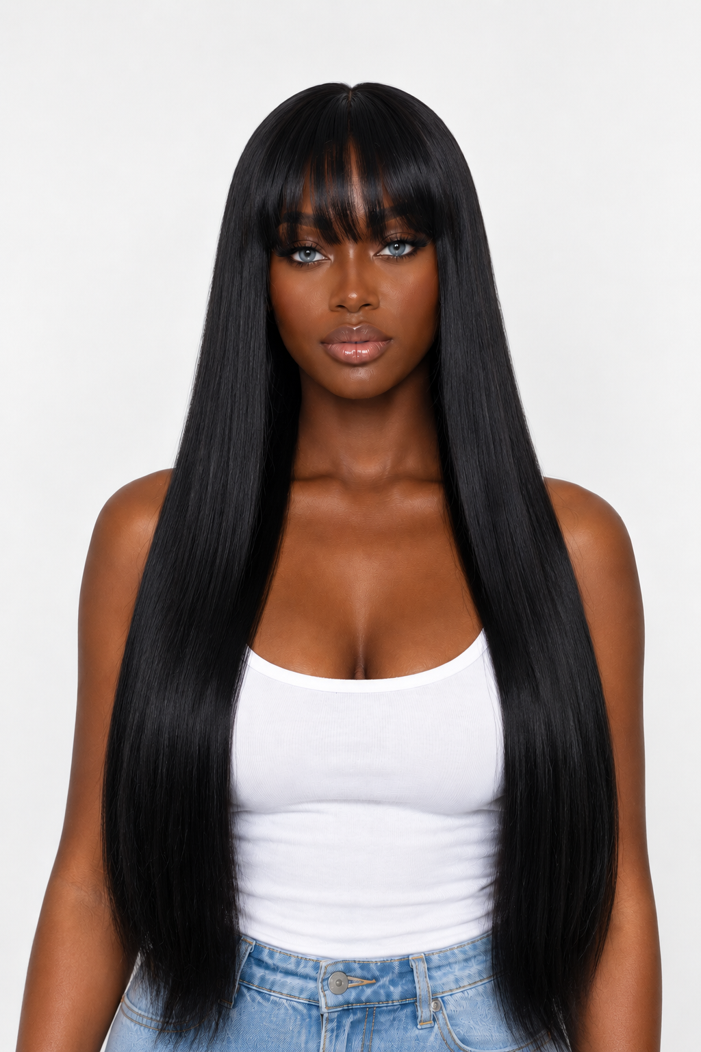 A woman with long, straight, black hair and straight bangs, wearing a white tank top and light blue jeans, photographed against a plain light gray background.