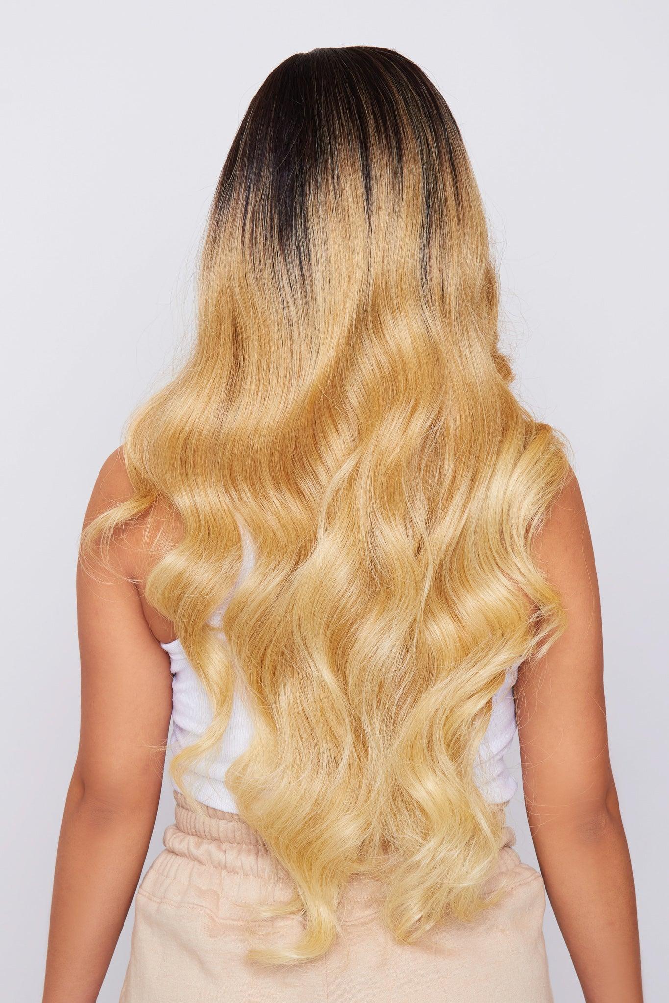 Long wavy ombre hair extension shown on a model from the back, featuring a dark brown root color that fades into a golden blonde.